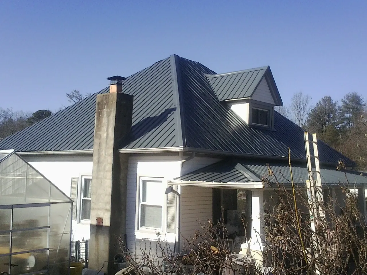 Dark blue standing seam metal roof on a white farmhouse with dormer — Slate & Tile Roof Repair by Roofing Brothers in Campbellsport