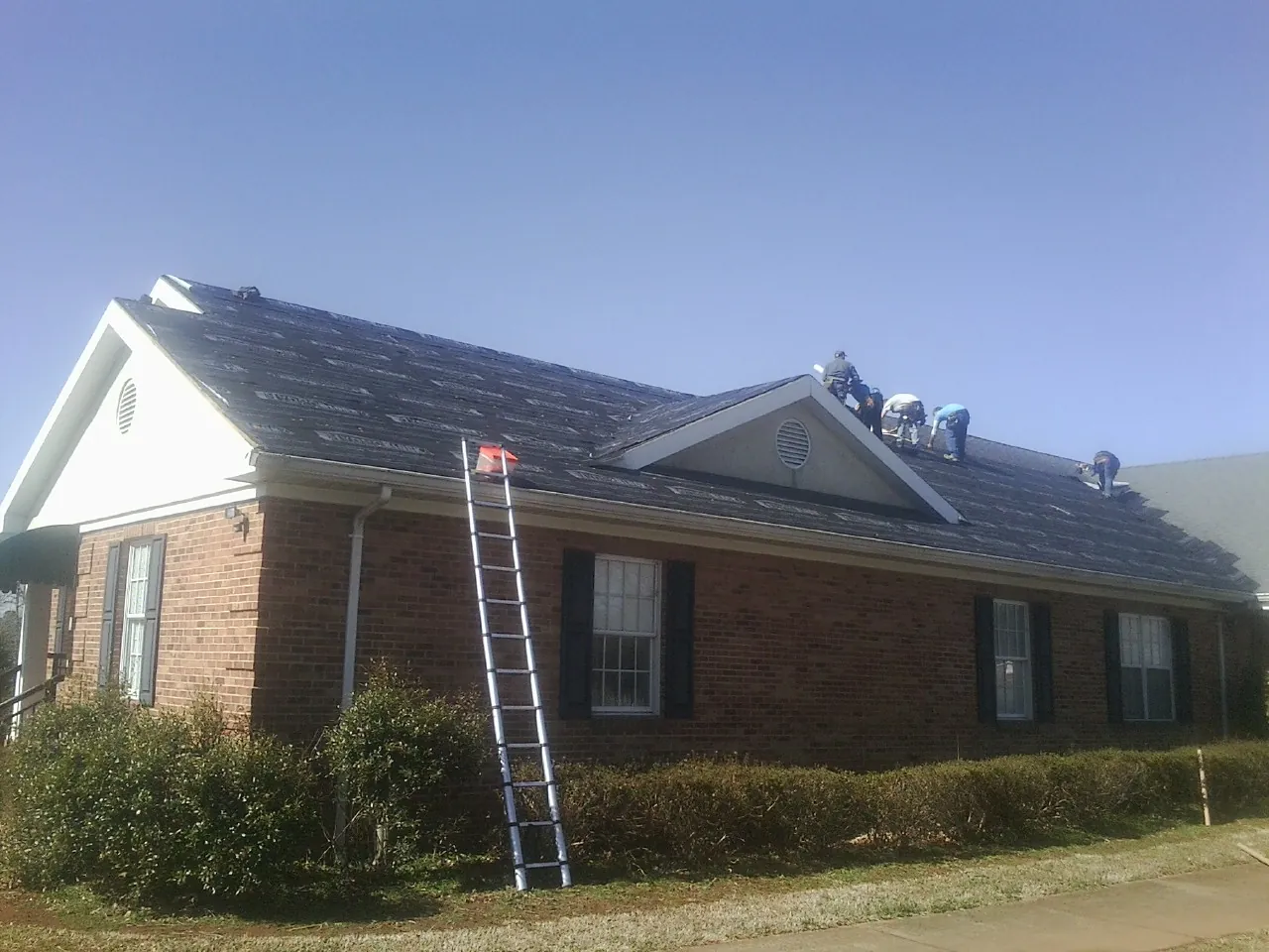 Crew tearing shingles off a brick ranch roof with a ladder set — Metal Roof Repair work by our crew in Campbellsport