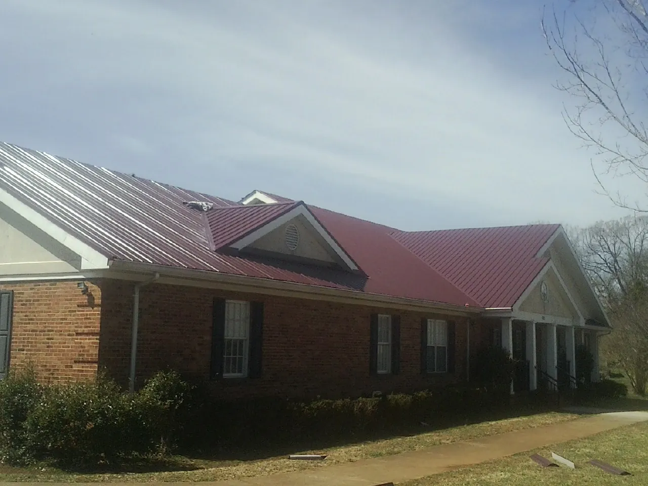 Red metal roof with gabled entries on a long brick building, from a Hail Damage Roof Repair job in Campbellsport