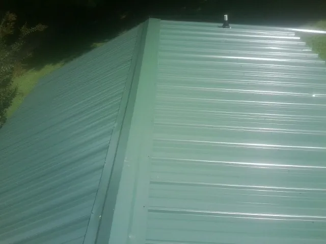 New green metal panels meeting at the ridge of a roof — Flat Roof Repair work by our crew in Campbellsport