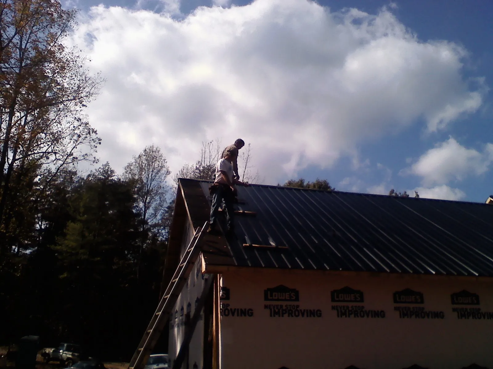 Roofer fastening dark metal panels high against a cloudy sky, from a Roof Inspection job in Campbellsport
