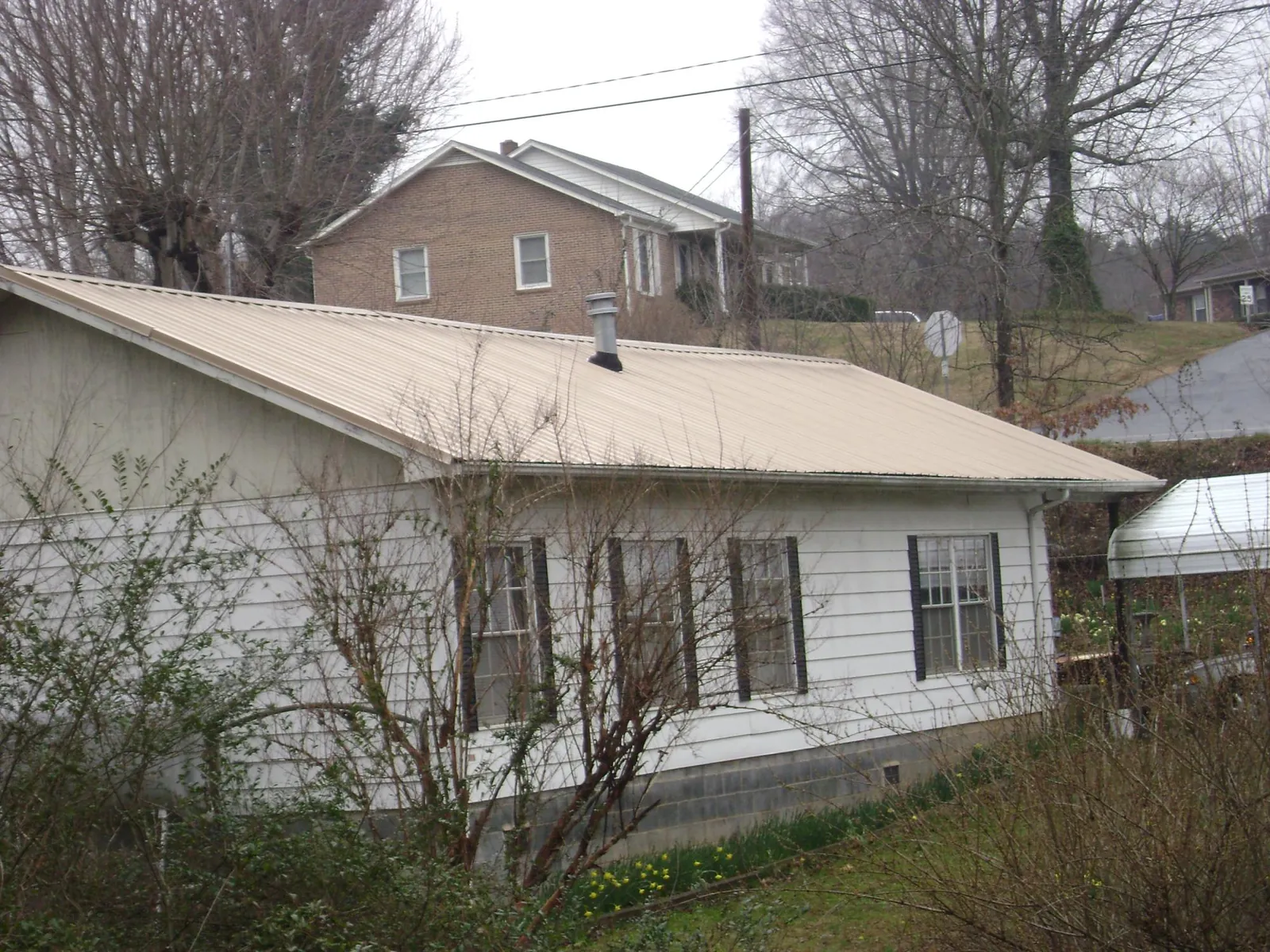 Tan metal roof on a white sided house set into a hillside — Commercial Roofing by Roofing Brothers in Campbellsport