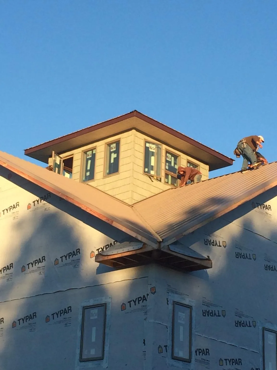 Roofers working around a rooftop cupola on a new metal roof at sunset — Roof Waterproofing in Campbellsport by Roofing Brothers